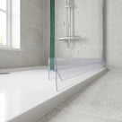 Clear seal along the bottom edge of a wet glass shower panel, fins spread onto a white tray