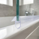 Clear bulb seal on the foot of a green-edged glass bath screen, round bubble resting on the white rim, taps behind