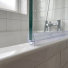 Clear seal on a bath screen bottom edge, small bubble squashed against the white bath rim