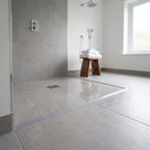 Clear threshold bead running across a grey tiled wet room floor, drain and teak towel stool behind