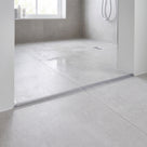 Semi-transparent threshold bead across a pale grey tiled wet room floor beside a glass shower panel