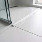 White threshold strip across a white tiled floor, glass screen edge to the left and water droplets
