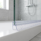 Clear seal along the bottom edge of a glass bath screen, water-speckled glass and shower rail behind