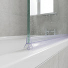 Clear bead-tipped seal along a wet glass bath screen resting on a white bath rim, chrome tap behind