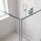 Two glass shower panels meeting at a right angle with a clear corner seal, tiled wall and chrome valve behind