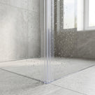 Clear seal in the vertical corner where two water-spotted glass shower panels meet, grey tiled walls behind