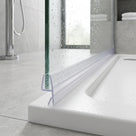 Clear seal along a wet glass shower panel edge on a white tray, chrome bath filler and towels behind