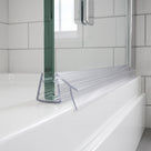 Clear seal with two angled blades at the foot of a glass bath screen on a white bath, metro tiles