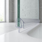 Clear deflector seal on the bottom edge of a glass shower screen over a white bath, droplets on the glass