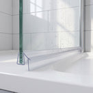 Clear seal with two angled blades along the foot of a wet glass shower door on a white tray
