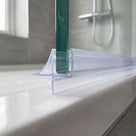 Clear seal along a glass screen bottom edge on a white tray, grey tiles and shower rail behind