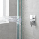 Clear join seal on wet glass panels meeting at a vertical edge, chrome shower valve on grey tiles behind