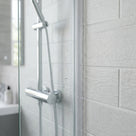 Clear seal down the vertical edge of a glass shower panel meeting pale grey wall tiles, chrome bar valve behind