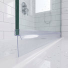 Clear seal with a long skirt along a glass screen bottom edge on a wet white tray, metro tiles