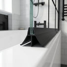 Black seal on a glass bath screen edge, wide fin sweeping onto the white bath rim, black shower fittings behind