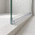 Clear seal with a wide flat fin fitted along the foot of a glass shower screen on a stone tray edge