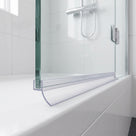Clear curved-blade seal along a glass door bottom edge on a white bath, white tiles behind