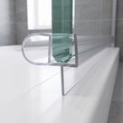 Clear seal with a side bubble along a glass screen bottom edge on a white bath, grey tiles behind