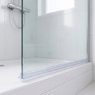Clear seal running the width of a glass screen bottom edge on a white bath, white tiles behind