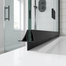 Black seal running along the foot of a glass shower panel on a white tray, black handles behind