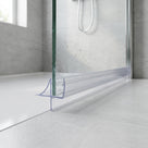 Clear seal with a long flat fin and a small hooked fin at the foot of a glass shower panel on a white tray