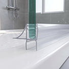 Clear seal at the foot of a glass panel on a white tray, curved flick fin above a long blade, chrome shower behind