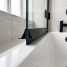 Black seal with a triangular deflector along the foot of a glass bath screen, black tap behind