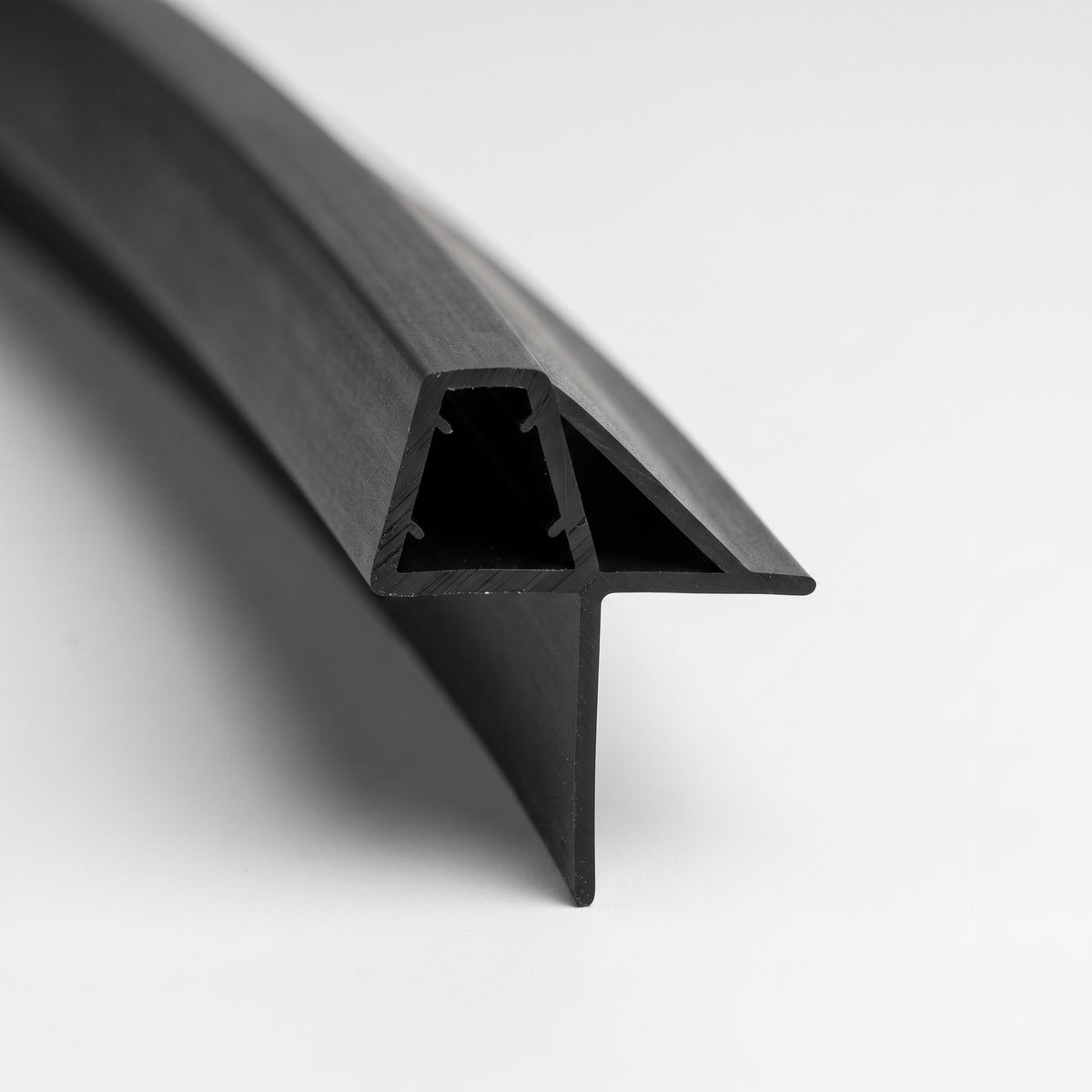 Length of black shower seal on white, glass channel with gripping nibs and a wide sloping wing