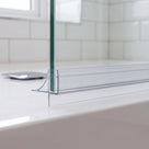 Clear seal along a glass screen bottom edge on a white bath, white metro tiles behind