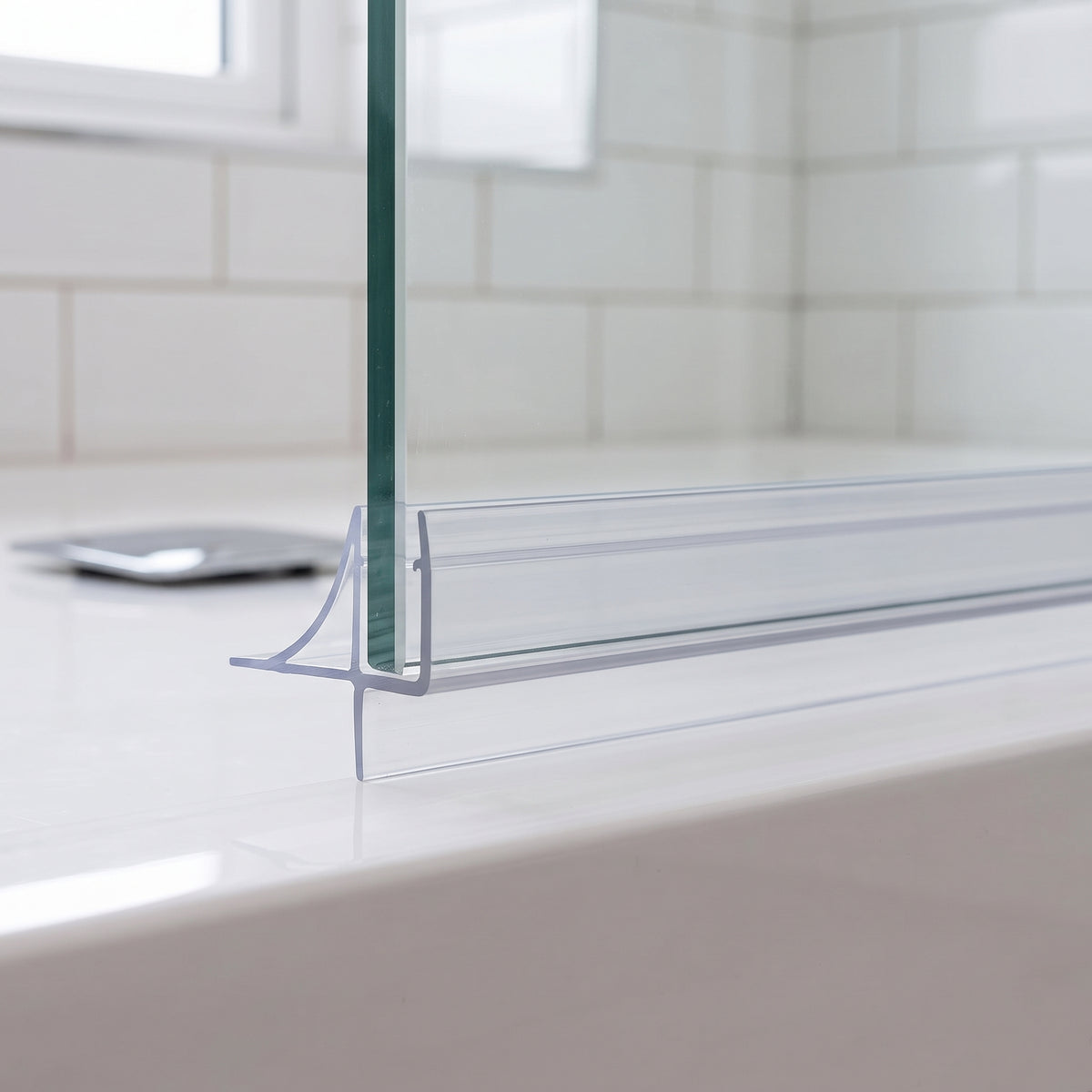 Clear seal along a glass screen bottom edge on a white bath, white metro tiles behind
