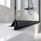 Black seal along a bath screen bottom edge on a white bath, grey marble-effect tiles behind