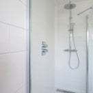 Glass shower screen in a white-tiled bathroom with a chrome riser rail, seal not visible here