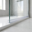 Clear seal along the bottom edge of a wet glass shower panel above a white tray, grey tiles behind