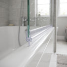 Clear carrier and T seal along the bottom of a wet glass bath screen on a white bath, window and grey tiles behind