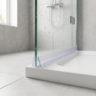 Clear seal at the foot of a green-edged glass screen on a white tray, fins either side, grey tiles behind