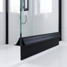 Black seal along the bottom of a wet glass shower panel on a white tray, black frame behind
