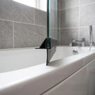 Black seal with an angled fin and long drop blade on a glass bath screen edge, over a white bath