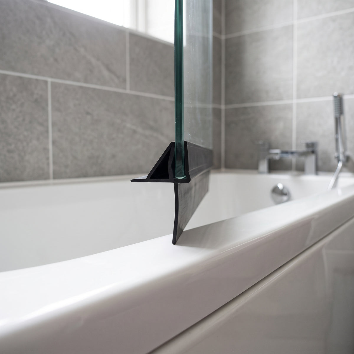 Black seal with an angled fin and long drop blade on a glass bath screen edge, over a white bath