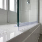 Clear seal running the width of a glass screen bottom edge on a white bath, tiled bathroom behind