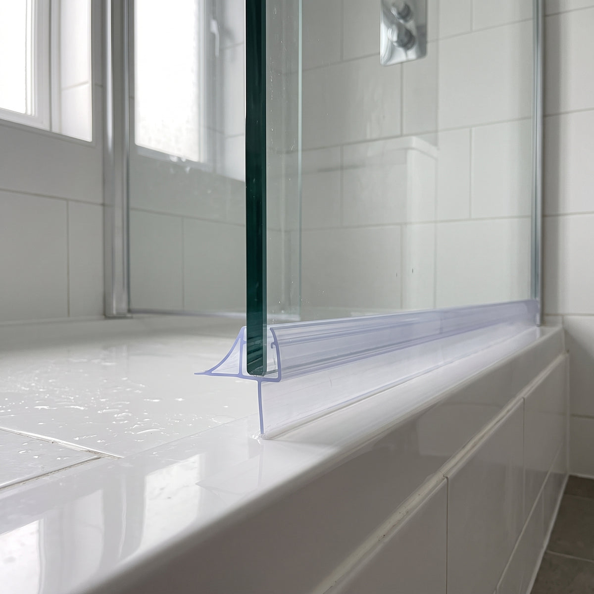 Clear seal running the width of a glass screen bottom edge on a white bath, tiled bathroom behind
