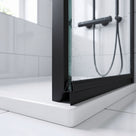Black seal at the foot of a wet glass shower door on a white tray, black frame and white tiles