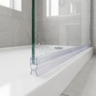 Clear seal along the bottom edge of a wet glass shower panel, twin legs resting on a white tray