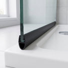 Black seal running along the foot of a glass shower screen on a white tray, chrome waste beyond