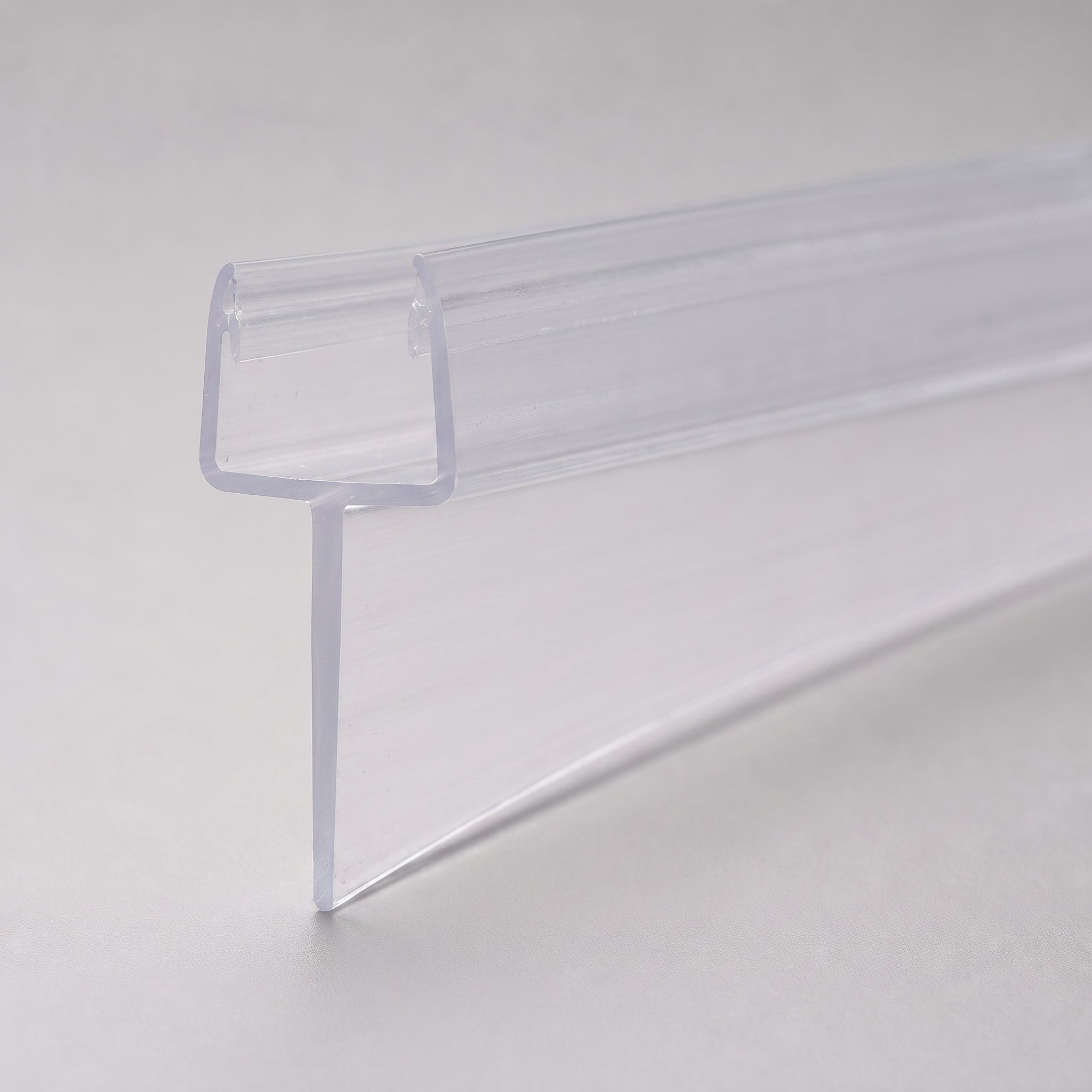 Studio shot of the tapered shower seal profile - clear PVC U-channel with fin tapering from 10mm to 5mm along its 900mm length