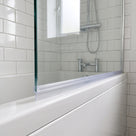 Clear tapered seal fitted along the bottom edge of a glass bath screen above a white bath, metro tiles