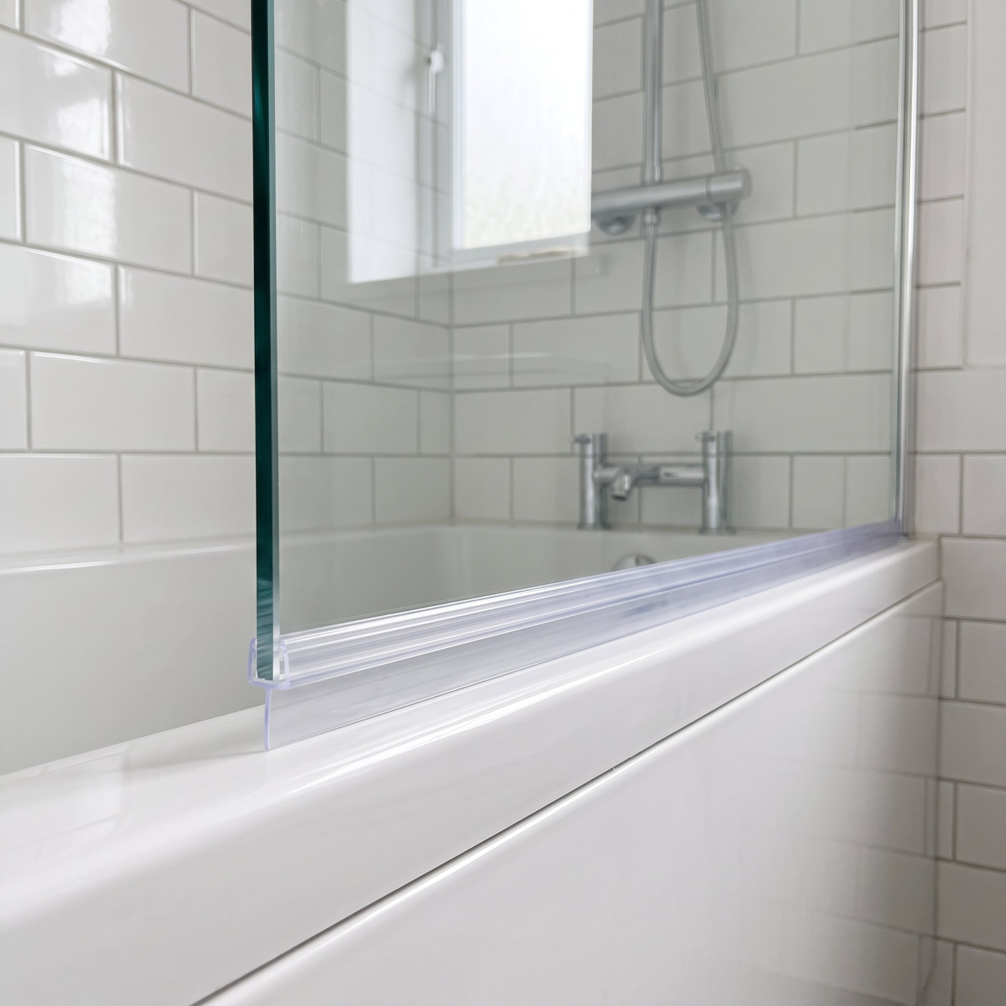 Clear SEAL166 tapered seal fitted horizontally along a bath screen bottom edge - deep fin end over the widest gap