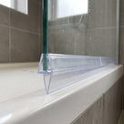 Clear tapered seal on the bottom edge of a glass screen over a white bath rim, brown tiles behind