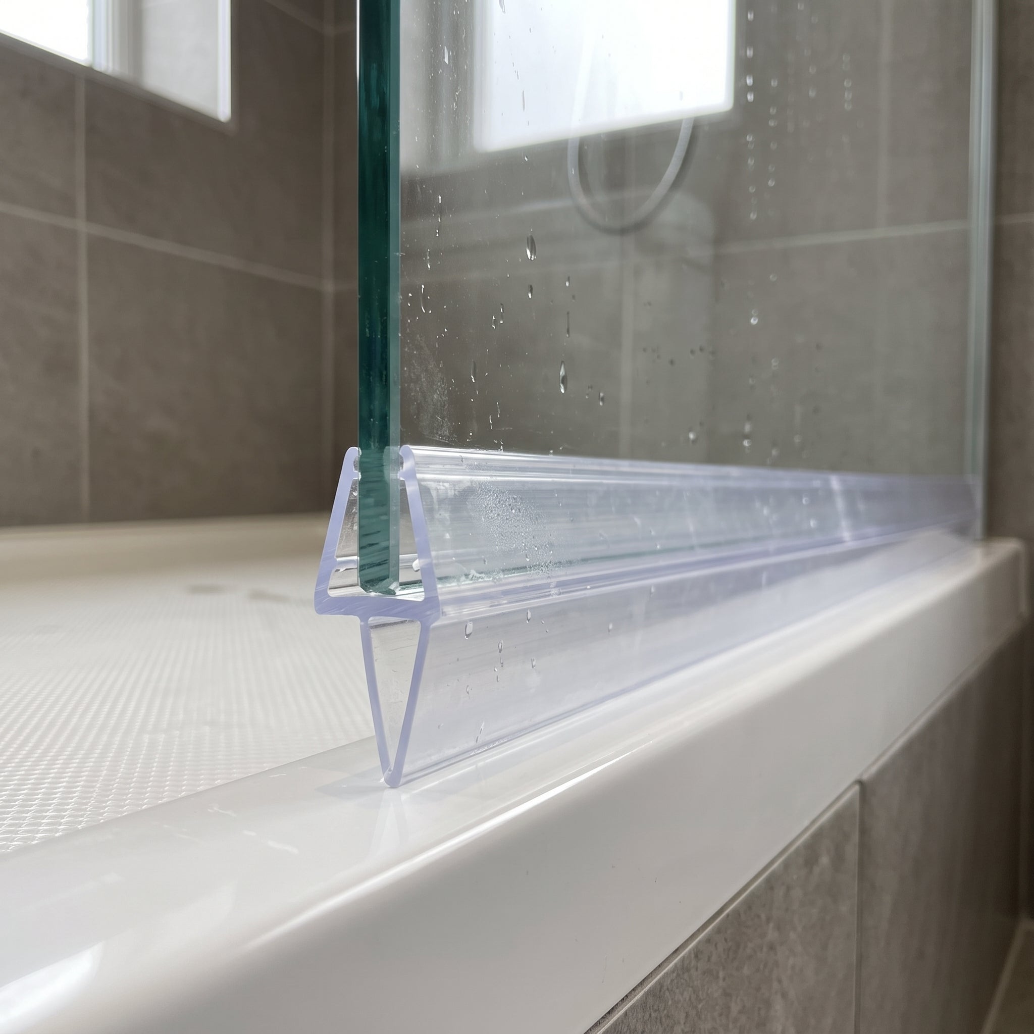 Tapered shower screen seal pushed onto the bottom edge of 4-6mm glass, clear fin tapering from 20mm to 5mm to close an uneven gap to the shower tray