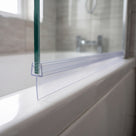 Clear tapered seal along the bottom edge of a glass bath screen, fin lying flat on the white bath rim