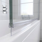 Clear tapered seal on a glass bath screen edge, fin sloping across the white bath rim, white tiles behind